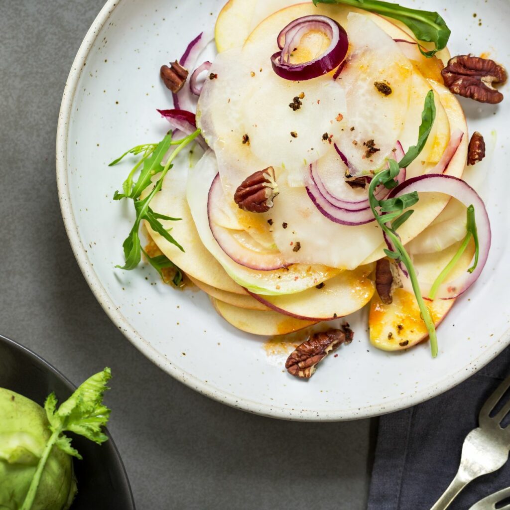 Kohlrabi-Apfel-Salat wird drappiert auf einem Teller serviert.