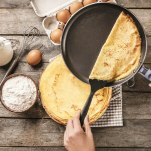 Pfannkuchen wird aus einer Pfanne gehoben und auf einen Stapel weiterer Pfannkuchen gelegt.
