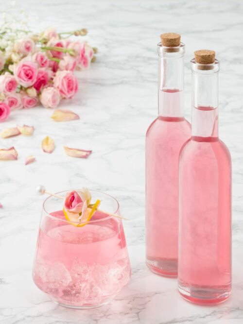 Rosensirup wird in zwei kleinen Flaschen und einem Glas mit Eiswürfeln präsentiert.