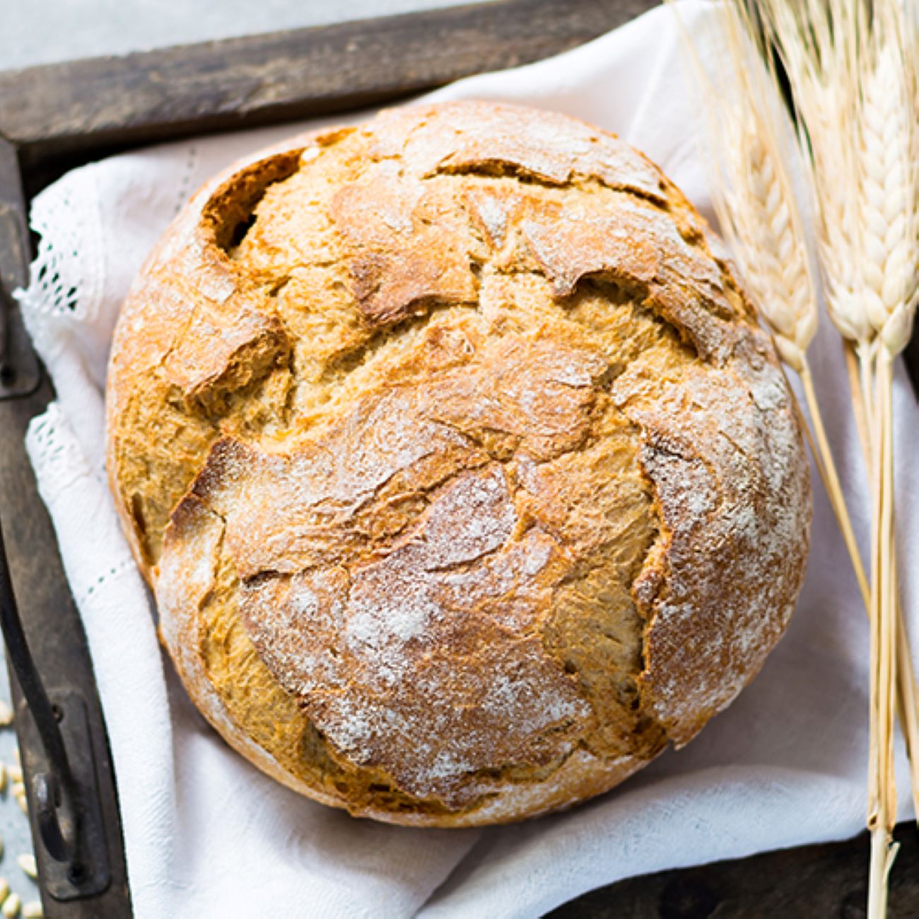 Pšenični kruh je prikazan od zgoraj na beli tkanini in okrašen s pšenico.