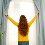 Tipps gegen Hitze: Frau öffnet Vorhänge