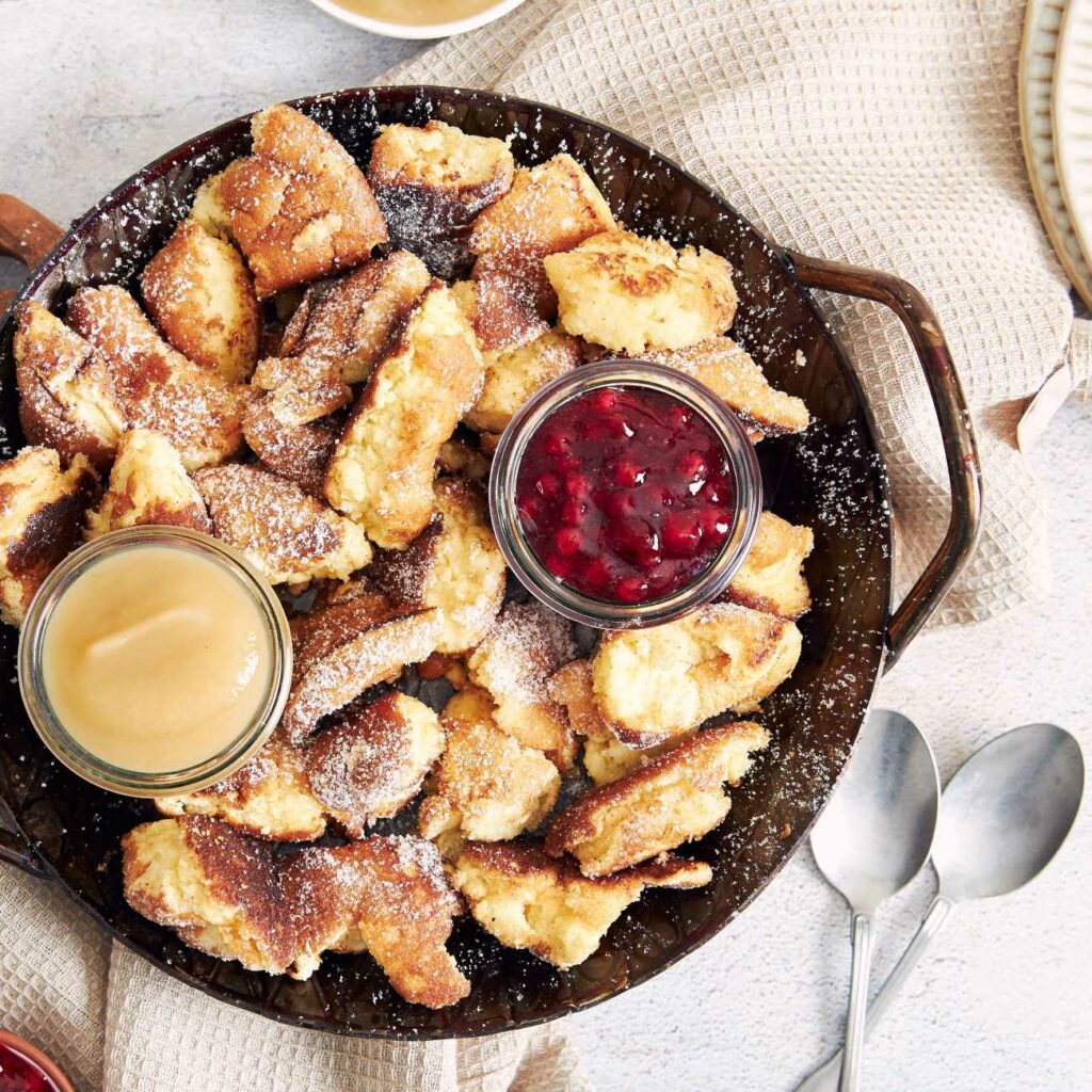 Kaiserschmarrn wird mit Kompott und Apfelmuss in einer schwarzen Pfanne serviert.