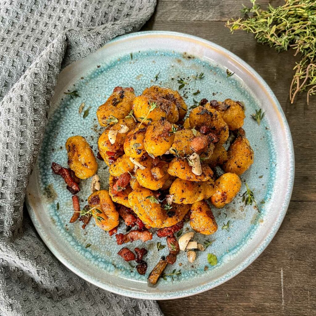 Kürbis-Gnocchi mit Thymian-Butter werden von oben auf einem blauen Teller gezeigt.
