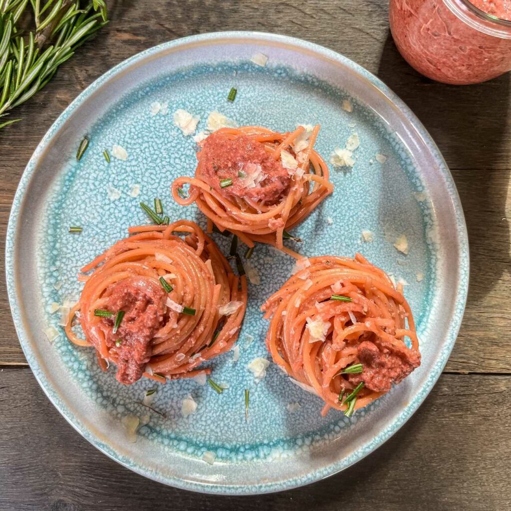 Rote Bete Pesto mit Spaghetti wird auf einem blauen Teller mit Rosmarin und Parmesan serviert.
