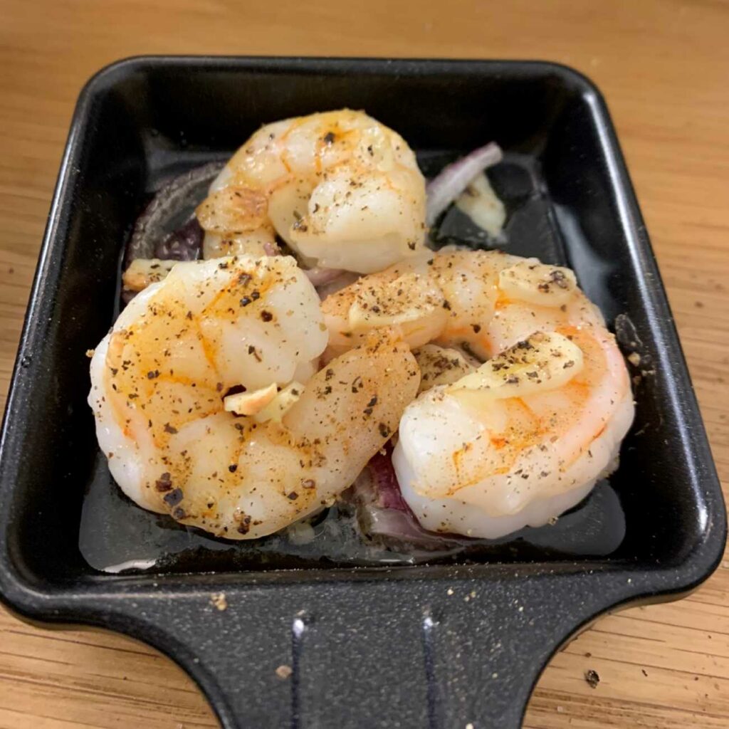 Garnelen-Raclette-Pfännchen wird in die Kamera gehalten.