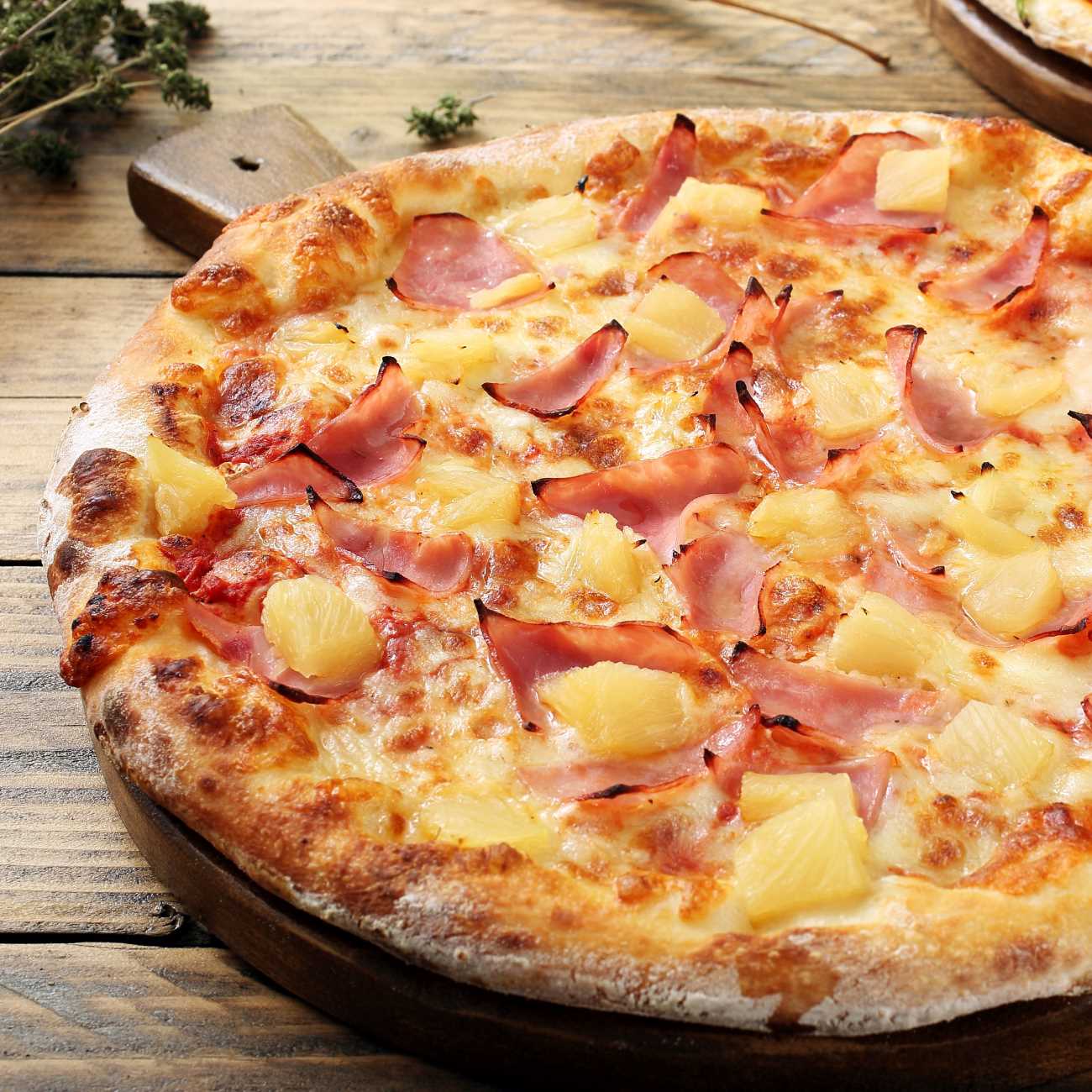 Pizza Hawaii wird auf einem runden Holzbrett serviert.