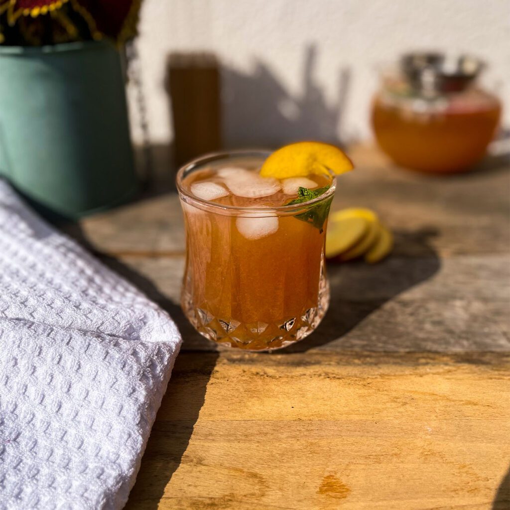 Eistee Pfirsich wird in einem Glas draußen in der Sonne gezeigt.